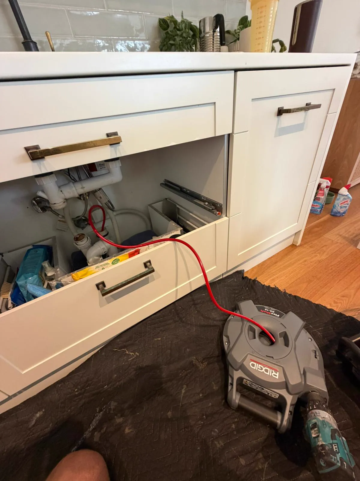 Clearing a blocked kitchen drain with a drain machine under the sink, Northern Beaches